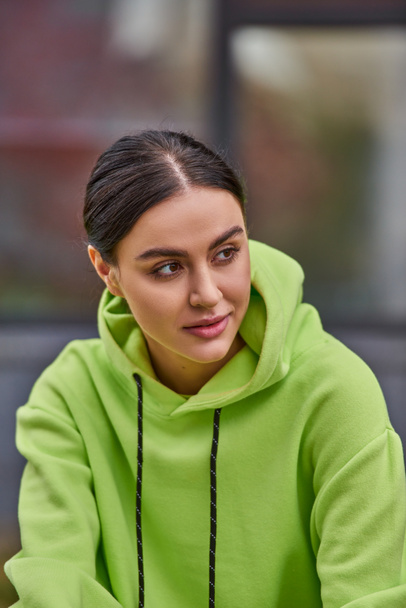 portrait of dreamy young woman with brunette hair in lime color hoodie looking away outdoors - Valokuva, kuva