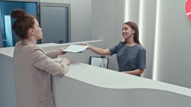 Jonge vrouwelijke patiënt heeft een afspraak in het moderne ziekenhuis ondertekening overeenkomst bij de receptie - Video