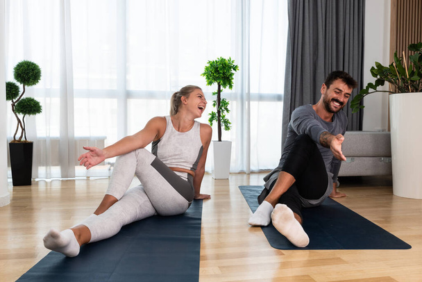 Couple exercising together. Man and woman in sportswear doing workout at home. Partners doing yoga class in the apartment on yoga mats stretching muscles breathing exercises after stress at work - Foto, Bild