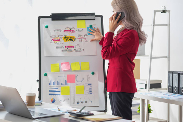 Asian businesswoman presenting a profitable company marketing plan with confidence at the office and future investment plans of the company with charts and graphs on the board. - Photo, Image