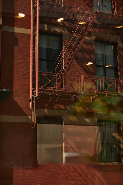 Sonbaharda New York şehrinde yangın merdivenleri ve gölgeleri olan klasik kırmızı tuğla bina. - Fotoğraf, Görsel