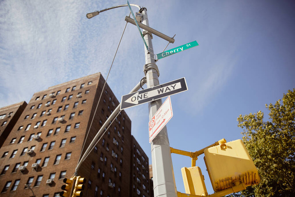 vista a basso angolo del palo della strada con cartelli stradali che mostrano la direzione vicino edificio in mattoni rossi a New York - Foto, immagini