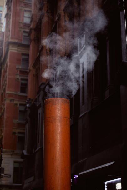 tubo di ventilazione fumante sulla strada vicino a edifici in pietra su sfondo sfocato nella città di New York - Foto, immagini