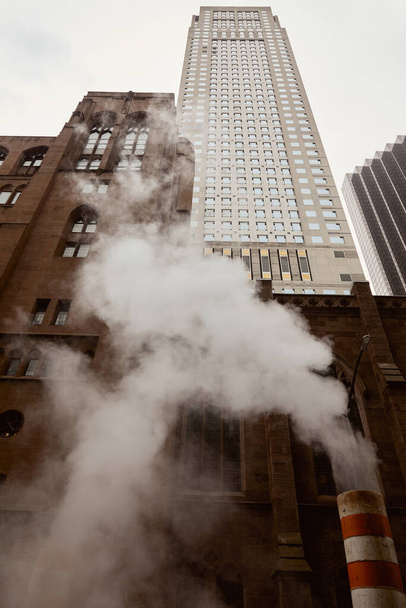 visão de baixo ângulo de tijolo vermelho igreja católica e arranha-céu perto de vapor na rua na cidade de Nova Iorque - Foto, Imagem