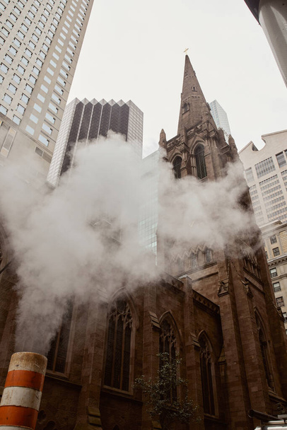 église catholique en brique rouge et gratte-ciel près de la vapeur sur la rue dans la ville de New York, vue à angle bas - Photo, image