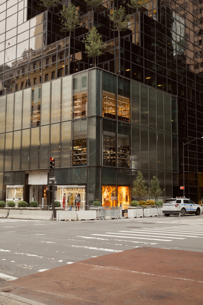 edificio moderno con fachada de vidrio y tienda de ropa en cruce en avenida en la ciudad de Nueva York - Foto, Imagen