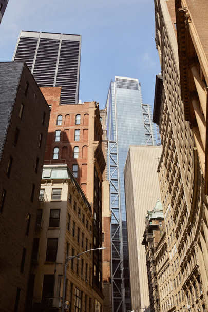 visão de baixo ângulo de arranha-céus modernos e edifícios vintage contra o céu azul na cidade de Nova Iorque - Foto, Imagem