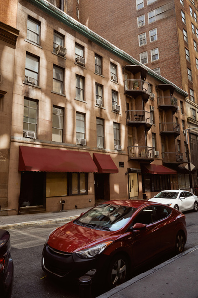 nowoczesne samochody zaparkowane w pobliżu kamiennych budynków na wąskiej jezdni przytulnej ulicy w Nowym Jorku, urok miasta - Zdjęcie, obraz