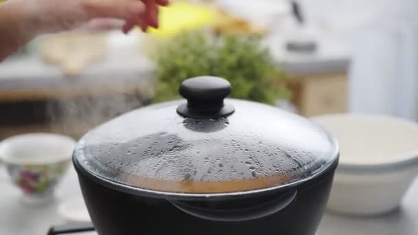Анонимный человек поднимает крышку сковороды и проверяет вкусное горячее рагу во время приготовления обеда в дневное время дома - Кадры, видео