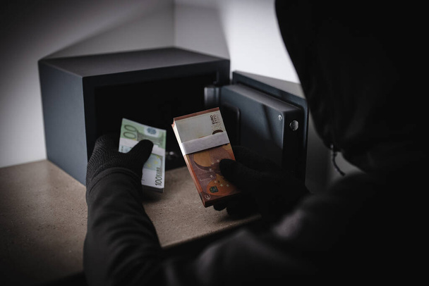 Κλέφτης κλέβει χρήματα από ένα ατσάλινο χρηματοκιβώτιο. - Φωτογραφία, εικόνα