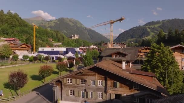 Bajo vuelo sobre chalets de madera en pequeño pueblo en valle entre montañas. Edificios rodeados de hermosos paisajes alpinos a la hora dorada. Gstaad, Suiza. - Metraje, vídeo