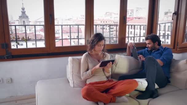 Νεαρό ζευγάρι με υπολογιστές tablet δύο στον καναπέ - Πλάνα, βίντεο