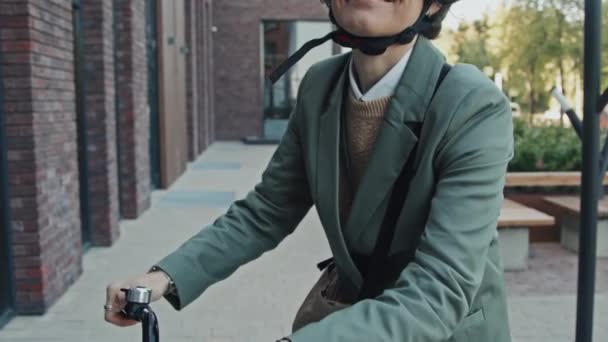 Inclinado retrato slow mo de la mujer moderna caucásica con el pelo rizado con ropa casual inteligente, gafas y casco de pie con la bicicleta sonriendo a la cámara - Imágenes, Vídeo