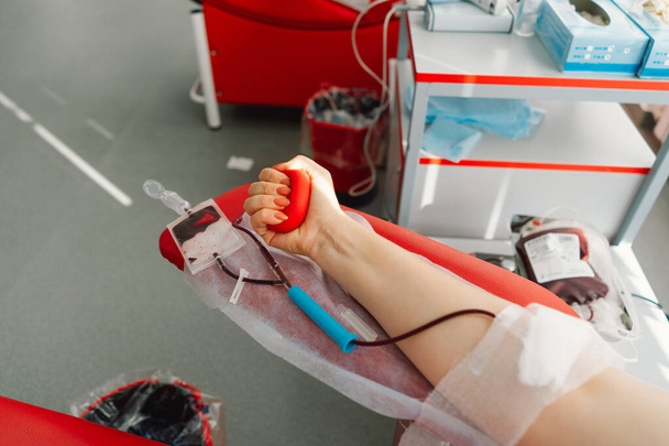 Νεαρή γυναίκα κάνει αιμοδοσία στο νοσοκομείο. Μια γυναίκα δωρίζει αίμα κρατώντας μια κόκκινη καρδιά. Αιμοδοσία. - Φωτογραφία, εικόνα