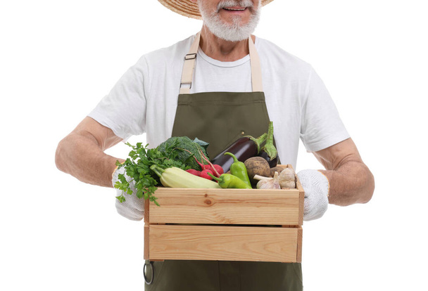 Harvesting season. Happy farmer holding wooden crate with vegetables on white background, closeup - Photo, image