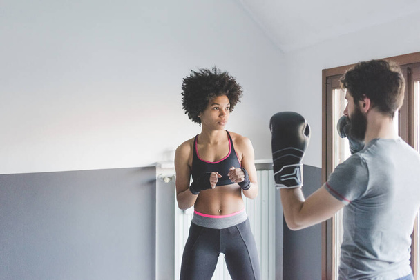 Молодая многонациональная женщина дома тренируется с тренером, занимающимся боксом - Фото, изображение