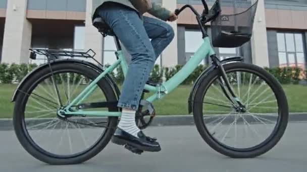 Dolly shot of legs of unrecognizable woman wearing jeans, loafers with striped socks cycling along street - Footage, Video