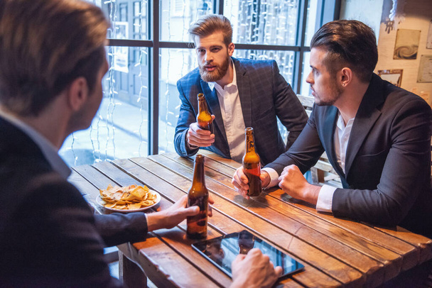 Красиві бізнесмени п'ють пиво, розмовляють і посміхаються, відпочиваючи в пабі
 - Фото, зображення