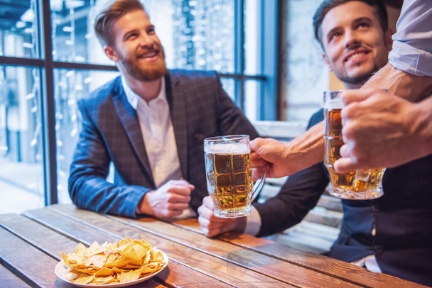 gutaussehende Geschäftsleute trinken Bier, reden und lächeln, während sie in der Kneipe ausruhen - Foto, Bild