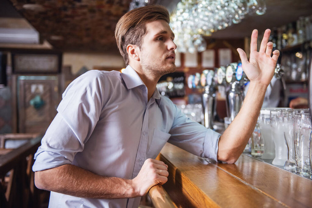 Bel giovanotto sta chiamando un cameriere mentre si trova al bancone del bar nel pub
 - Foto, immagini