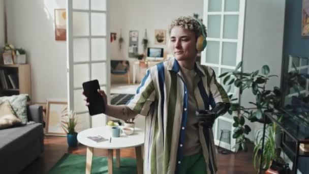 Μέτριο πλάνο της γυναίκας με αναπηρία, που φοράει κομψά αιτιολογικά ρούχα ακούγοντας μουσική στα ακουστικά και χορεύοντας στο σαλόνι - Πλάνα, βίντεο