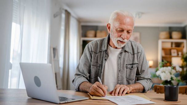 starszy kaukaski mężczyzna list otwarty list podpis koperta dokument podczas siedzieć przy stole w domu otrzymując wyciąg bankowy kredyt zatwierdzenia umowy lub zaproszenie do ubezpieczenia biznesu - Zdjęcie, obraz