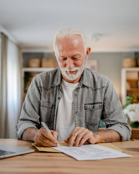 senior caucasian man open mail letter sign document envelope while sit at the table at home receiving bank statement loan approval contract or business insurance news invitation - Photo, Image