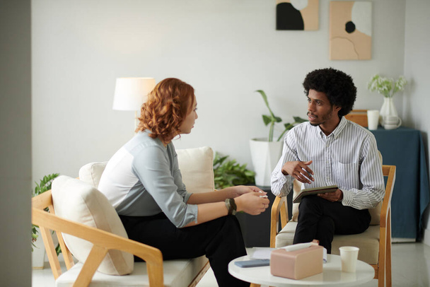 Σοβαρός ψυχοθεραπευτής μιλάει με πελάτη στο γραφείο του - Φωτογραφία, εικόνα