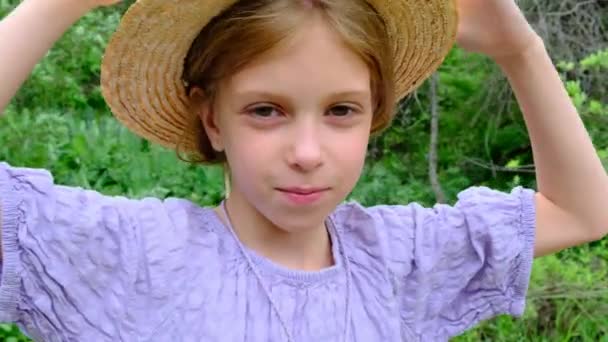  Dziewczyna w słomkowym kapeluszu patrząca w kamerę przeciwko zielonej naturze. Wysokiej jakości materiał 4k - Materiał filmowy, wideo