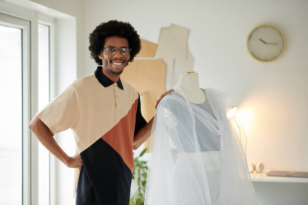Hymyilevä Musta muotisuunnittelija seisoo vieressä mallinukke draped kangas - Valokuva, kuva