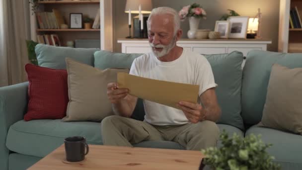 старший кавказький чоловік відкриває поштовий лист або документ конверт, сидячи за столом вдома, отримуючи кредитну заяву про схвалення банку або бізнес-страхування новини запрошення повільний рух - Кадри, відео