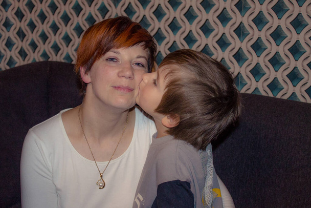 Мальчик целует мать в щеку. Женщина получает кисть от ребенка с улыбкой - Фото, изображение