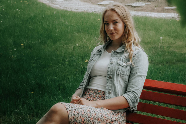 Une jeune femme s'assoit sur un banc rouge et regarde dans la caméra. La fille apprécie la belle nature. Concentration sélective douce - Photo, image