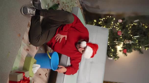 Тисячолітній чоловік у капелюсі Санта страждає від нудоти та похмілля після вечірки на Різдво. Концепція отруєння та алкогольної залежності. Вертикальне відео - Кадри, відео
