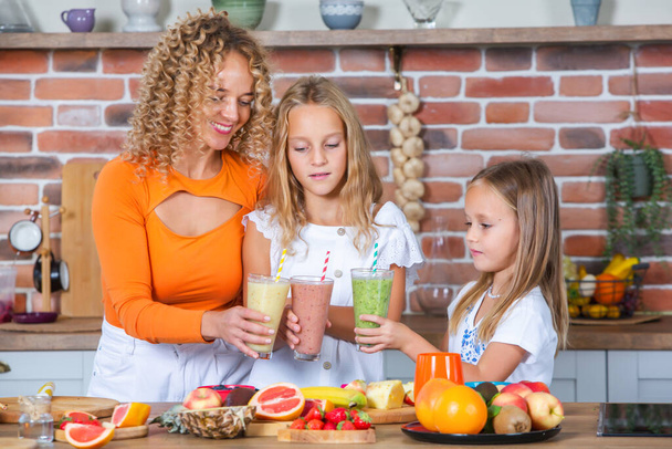 Mother and daughters cooking together in the kitchen. Healthy food concept. Portrait of happy family with fresh smoothies. Happy sisters. - Photo, Image