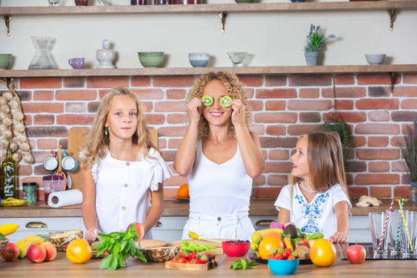 Moeder en dochters koken samen in de keuken. Gezond voedsel concept. Portret van een gelukkig gezin met verse smoothies. Gelukkige zussen. - Foto, afbeelding