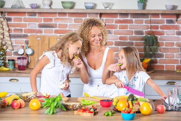 Matka i córki gotują razem w kuchni. Koncepcja zdrowej żywności. Portret szczęśliwej rodziny ze świeżymi smoothies. Szczęśliwe siostry. - Zdjęcie, obraz