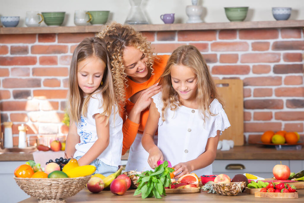 Moeder en dochters koken samen in de keuken. Gezond voedsel concept. Portret van een gelukkig gezin met verse smoothies. Gelukkige zussen. - Foto, afbeelding