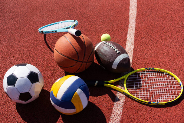 Una variedad de equipos deportivos que incluyen un fútbol americano, una pelota de fútbol, una raqueta de tenis, una pelota de tenis y una pelota de baloncesto. - Foto, imagen