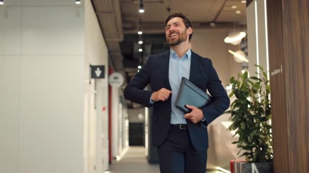 Dynamische corporate executive arriveert op kantoor met stralende glimlach, vrolijk zwaaien hallo aan collega 's en het delen van uitstekende stemming. Zorgeloze man van middelbare leeftijd die positieve emoties uitdrukt. - Video