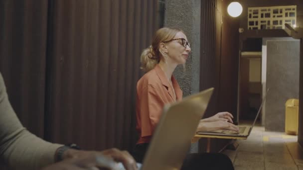 Ampliar la toma de diversos hombres y mujeres utilizando sus computadoras portátiles en pequeñas mesas de trabajo mientras trabajan de forma remota en una cafetería independiente con un interior elegante - Imágenes, Vídeo