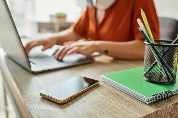 обрізаний зосереджений вид мобільного телефону на столі поруч з розмитою жінкою, яка навчається в ноутбуці, освіта - Фото, зображення