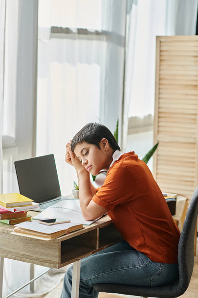 vertikale Aufnahme eines jungen nachdenklichen Schülers, der am Tisch sitzt, während er Online-Unterricht, Bildung besucht - Foto, Bild