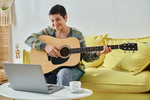 vrolijke vrouw zitten op de bank met gitaar wonen online muziekles, onderwijs thuis - Foto, afbeelding