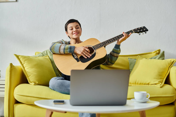 Радостная привлекательная женщина в повседневной одежде на онлайн-уроке игры на гитаре, обучение дома - Фото, изображение