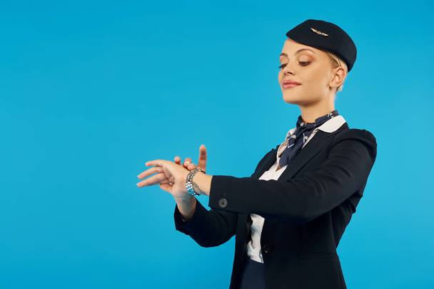 νεαρή κομψή κυρία με στολή αεροσυνοδού χρόνο ελέγχου για ρολόι χειρός σε μπλε, ακρίβεια - Φωτογραφία, εικόνα