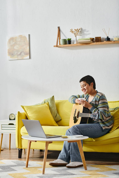 κάθετη βολή της νεαρής χαμογελαστή γυναίκα σε απομακρυσμένο μάθημα κιθάρας κάθεται στον καναπέ, εκπαίδευση στο σπίτι - Φωτογραφία, εικόνα