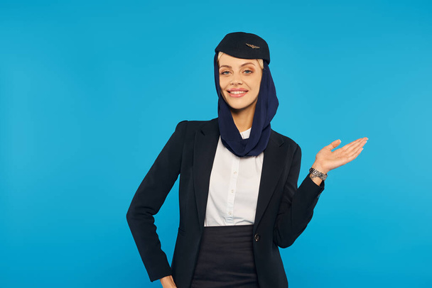arabian Airlines hospitalité, hôtesse souriante en foulard et uniforme montrant la direction sur bleu - Photo, image