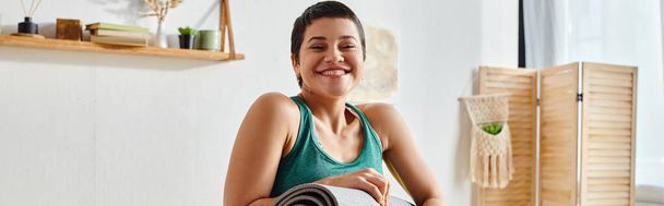 Spor giyinen neşeli kadın kameraya gülümsüyor ellerinde spor paspası, spor ve spor, afiş - Fotoğraf, Görsel