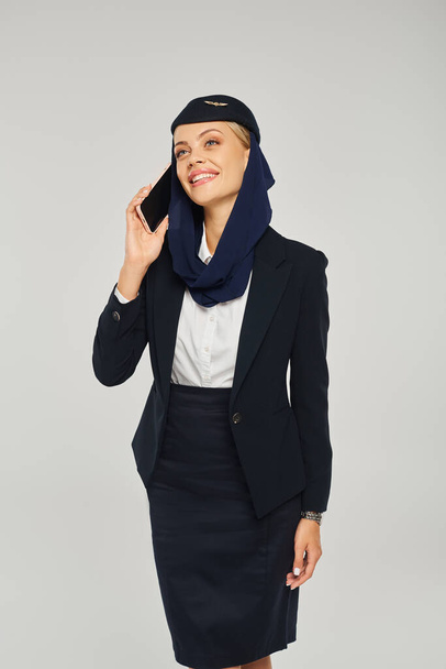 усміхнена стюардеса в арабських авіакомпаніях форма розмовляє на смартфоні і дивиться в сторону сірого - Фото, зображення